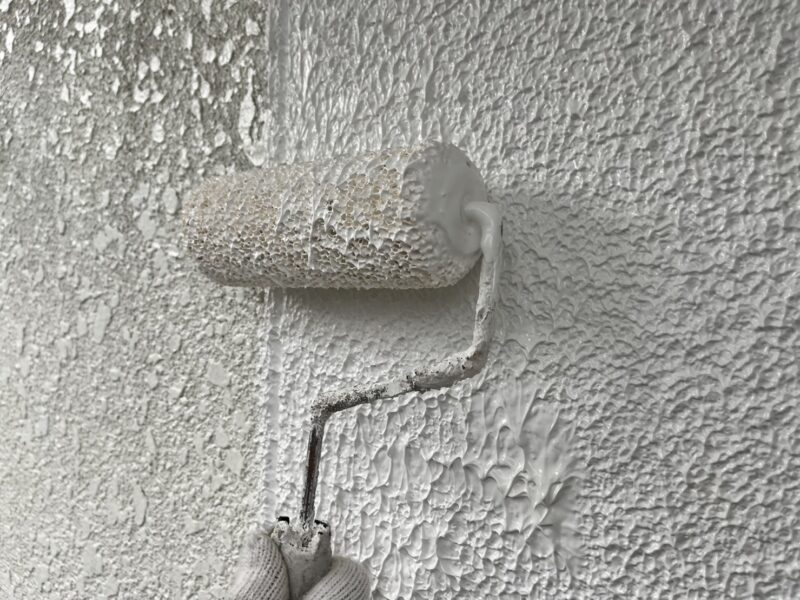 外壁下塗りの様子です。<br />ヒビ割れが多かったため、マスチックローラーという少し太めのローラーを使います。<br />使用塗料は「リメークプラ」で、凹凸をなくしたり、ヒビ割れを埋めたりでき、さらにその上に塗る塗料のノリを良くしてくれます。